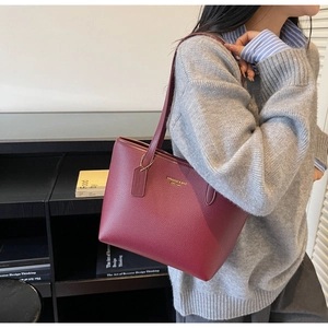 Detail of burgundy lychee grain leather tote bag with gold logo and matching shoulder strap