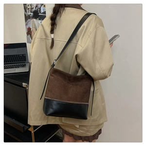Detail view of large brown suede and black leather tote bag worn by a model in office