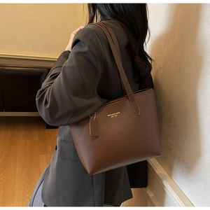 Close-up of brown pebbled leather tote bag with gold logo on a female model shoulder