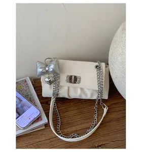 Detail of creamy white pleated bag featuring chunky silver chain and metallic heart charm