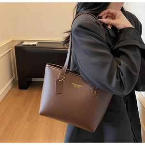 Brown pebbled leather tote bag worn by a model, showing large capacity and brand detail