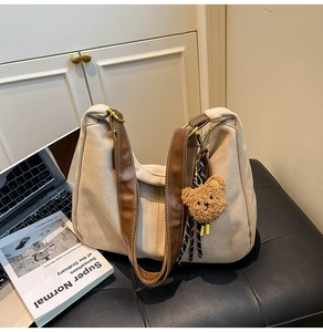 Detail shot of a beige suede dumpling bag with brown leather strap and a cute bear charm