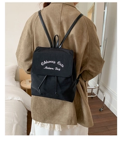 Détail d'un sac à dos en toile noire avec broderie blanche E&honey et rabat à cordon