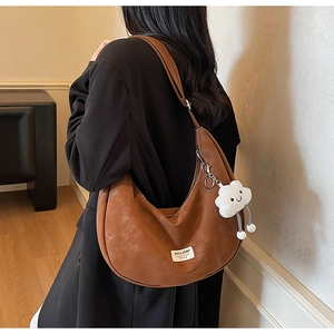 Detail of brown leather crescent bag with white stitching and plush cloud pendant accessory