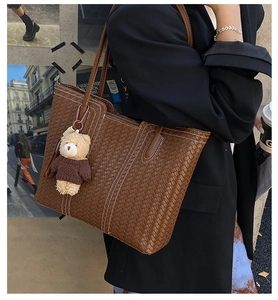 Brown woven leather tote bag shown in a stylish street setting with a cute bear charm