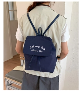Détail du sac à dos en nylon bleu foncé avec broderie blanche et rabat à cordon serré
