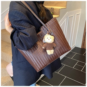 Detailed view of brown woven leather tote bag with a small bear charm and white stitching