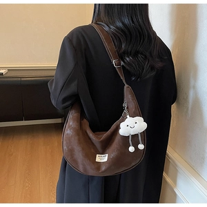 Detail of dark brown crescent bag with vintage matte leather and white plush charm