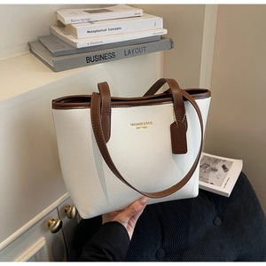 Close-up of white pebble leather tote bag with brown trim and gold brand lettering