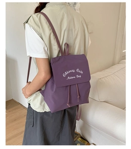 Détail du sac à dos en nylon violet avec fermeture à cordon et broderie blanche