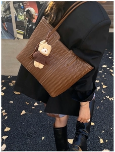 Detail of vintage brown woven tote bag with contrast stitching and cute bear charm