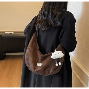 Detail view of large brown hobo crossbody bag with white cloud plush pendant