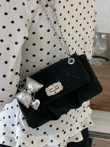 Chic black textured crossbody bag with silver chain strap and bow pendant detail