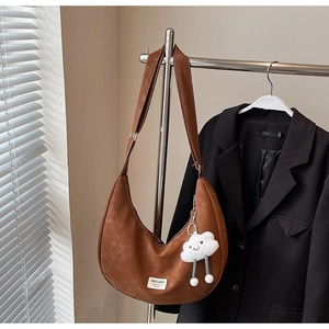 Detail of brown vintage leather hobo bag with a soft white cloud charm and wide strap