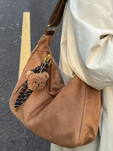 Brown suede hobo shoulder bag with bear charm in a stylish outdoor street style scene