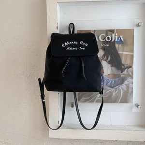 Détail d'un sac à dos en toile noire avec rabat, broderie blanche et bretelles réglables