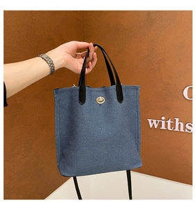 Détail d'un mini sac cabas en denim bleu avec fermoir rotatif doré et anse en cuir noir