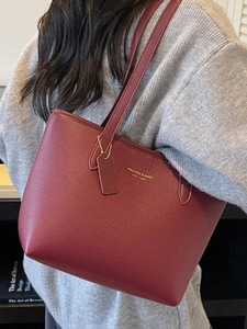 Large red pebbled leather tote bag with gold lettering shown on a female model shoulder