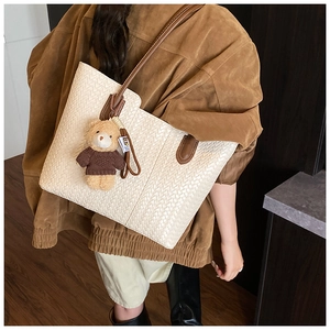 Detail of large woven leather tote bag with brown handles and a cute bear charm pendant