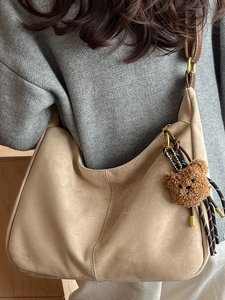Minimalist beige suede crossbody dumpling bag with brown leather strap and bear charm