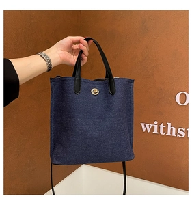 Détail d'un sac en jean bleu avec poignées en cuir noir et fermoir rotatif doré élégant