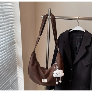 Detail of dark brown leather hobo bag with logo patch and plush cloud pendant