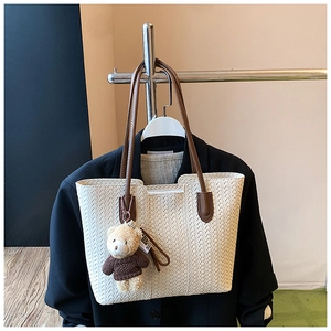 Detail of a cream woven tote bag with brown leather straps and a cute teddy bear charm
