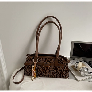 Detail view of leopard print shoulder bag with brown leather trim and beaded charm on a desk