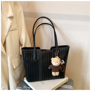 Detail of black woven leather tote bag with white contrast stitching and a cute bear charm