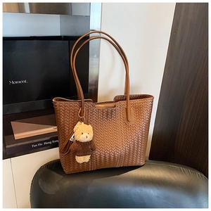 Detail of a brown woven tote bag with a long leather strap and a cute teddy bear charm