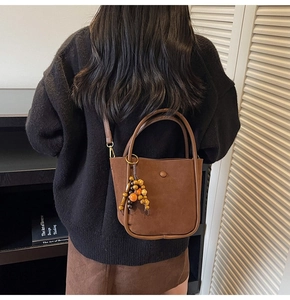 Detail view of large brown faux suede bucket bag with vintage wooden bead pendant accessory