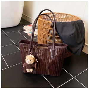 Detail of dark brown woven tote bag with leather straps and a cute plush bear pendant