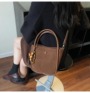 Detail of suede bucket bag with leather handles and decorative wooden beads