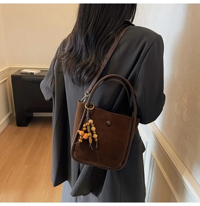 Detail of a dark brown suede bucket bag with leather strap and ethnic wood bead charm