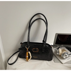 Close-up of black leather shoulder bag with gold logo and decorative beaded charm