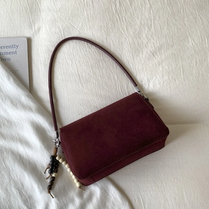 Detail of burgundy suede shoulder bag with retro wooden bead tassel on white fabric