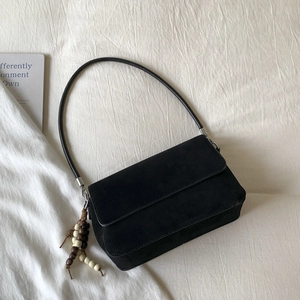 Detailed close-up of a black suede handbag featuring a retro wooden bead charm accessory