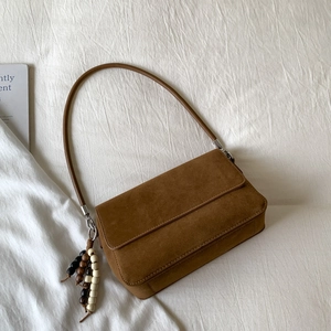 Detail view of brown faux suede shoulder bag with decorative wooden beads on white fabric