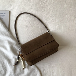 Detail of dark brown suede shoulder bag featuring chic beaded tassel on white fabric