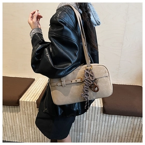 Side view of beige minimalist underarm bag with decorative strap and letter charm on model