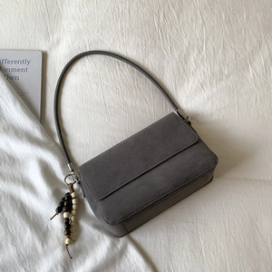 Close-up of minimalist grey suede shoulder bag with decorative beaded tassel on white fabric