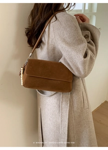Detail of brown suede shoulder bag with wood bead tassel on cream background