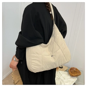 Detail of light beige quilted nylon tote bag featuring a magnetic snap button closure