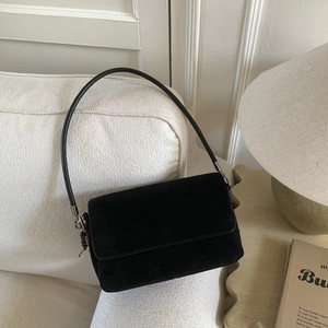 Detail shot of black suede shoulder bag on a cozy fabric sofa in a warm home setting