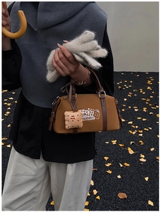 Brown Boston bag detail with retro embroidery and cookie plush charm on autumn leaves background