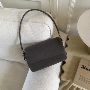 Detail of dark grey suede leather shoulder bag resting on a white textured sofa