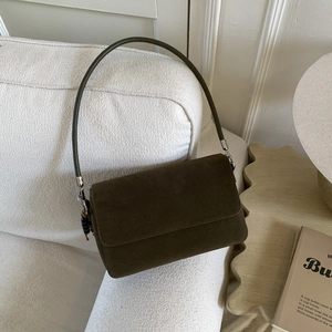 Detail of suede flap bag with silver buckle and black bead charm on a beige sofa