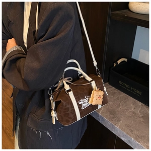 Detail view of leopard print Boston bag with white leather straps and plush cookie charm