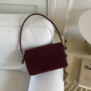 Detail of burgundy suede shoulder bag with minimalist flap design and silver hardware