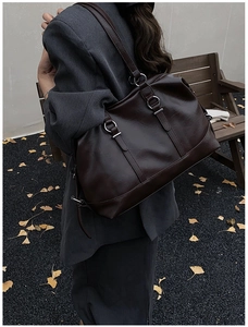 Detail of dark brown vintage leather tote bag with silver hardware on a wooden park bench